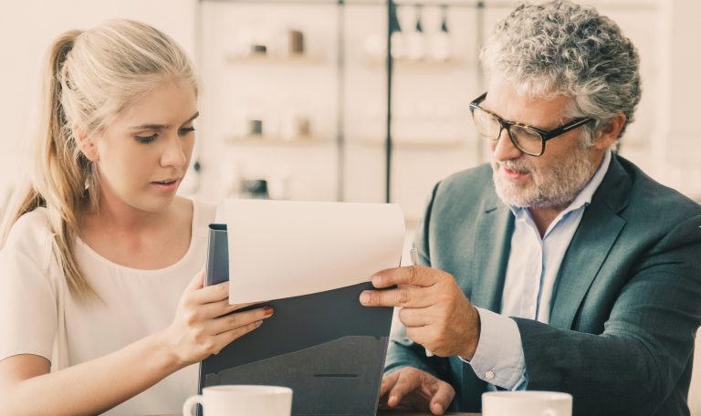 Dojrzały doradca prawny czytający dokument i wyjaśniający szczegóły młodemu klientowi